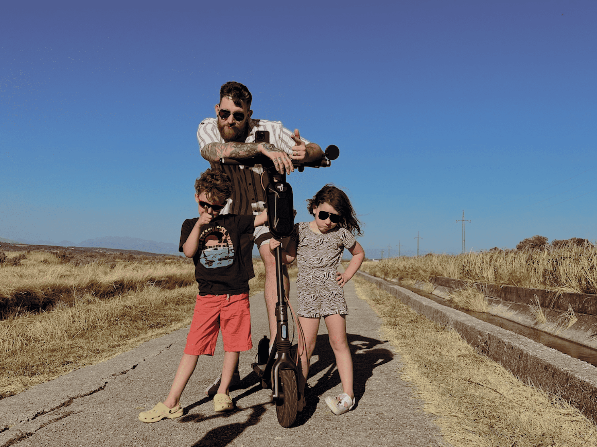 Family posing outdoors with electric scooter during travel prep — parent with two children