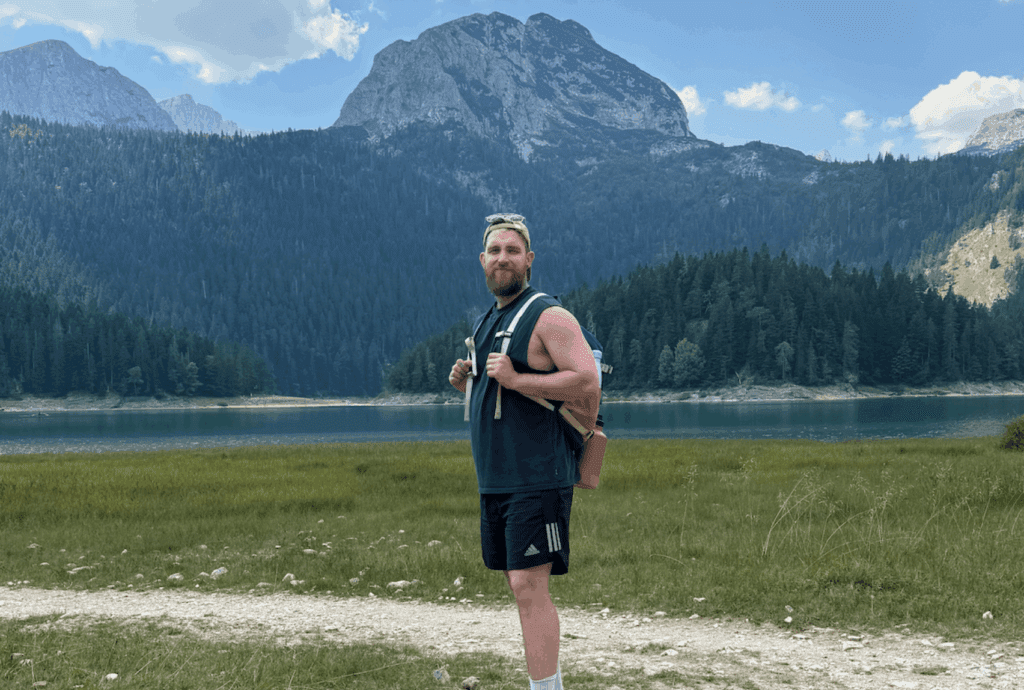 Dad standing with backpack in front of Montenegro’s Black Lake and forested peaks — family hiking trail