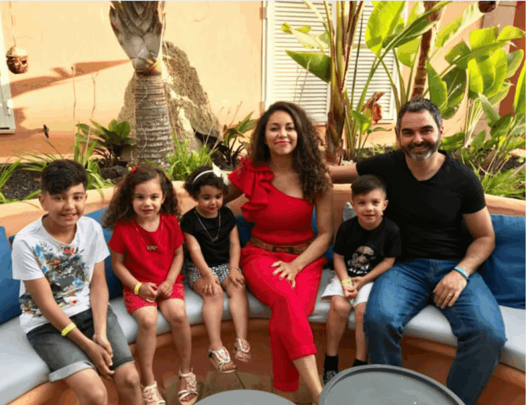 Multicultural family of six smiling together on a sunny terrace — Meet the Arshads, creators of a top family travel blog in 2025.