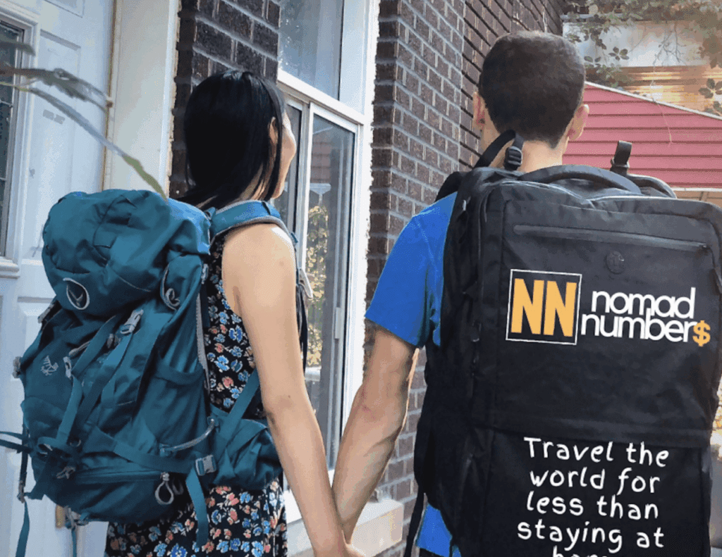 Couple wearing large backpacks with Nomad Numbers branding, holding hands outside their home