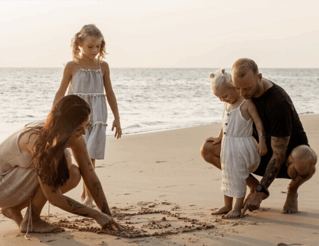 Young family on the beach at sunset, drawing in the sand together