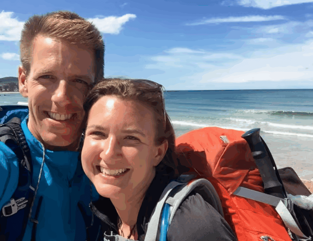 Audrey and Daniel from Uncornered Market smile with backpacks by the beach, promoting responsible and immersive travel.