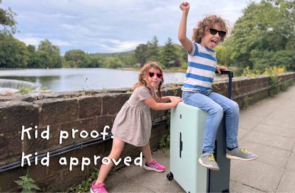 Kids playing with mint green suitcase near scenic water