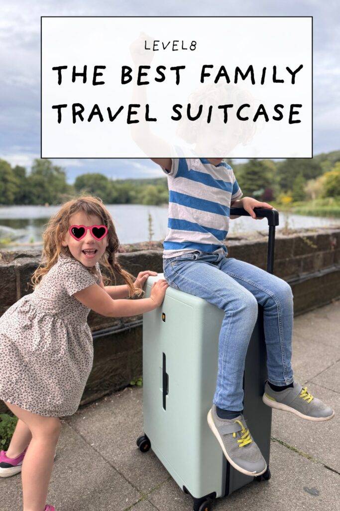 Two kids sitting and playing on a mint Level8 suitcase by a lakeside path
