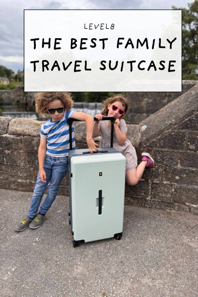 Young siblings posing with a Level8 suitcase on a stone bridge with waterfall backdrop