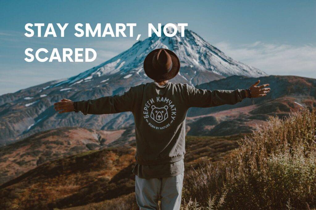 Traveler with arms wide facing a mountain, text ‘Stay Smart, Not Scared’—family travel safety mindset.